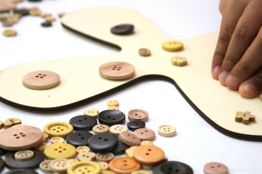 child arranging wooden buttons on a wood cross