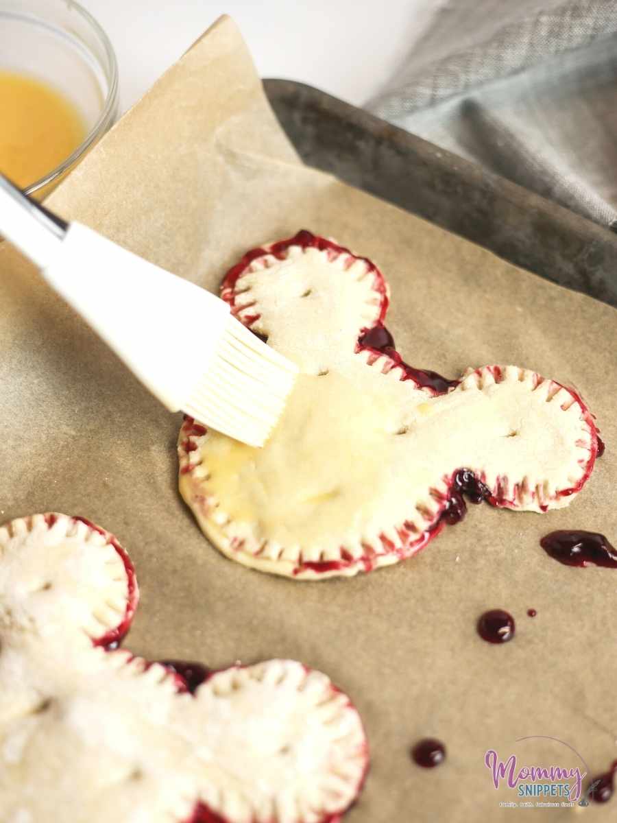 covering each cherry turnover with egg wash before popping them into the oven