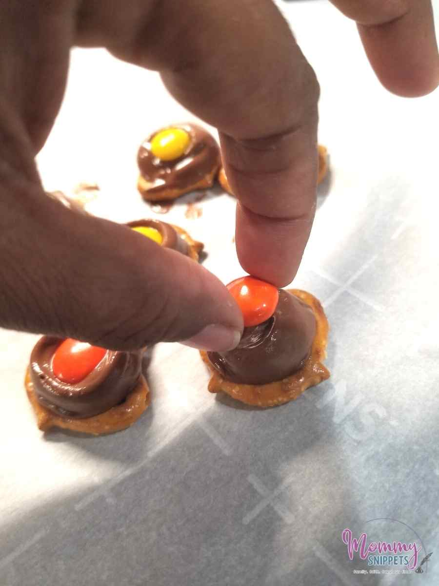 placing an M&M on a Rolo for pretzel treats